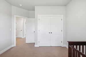 Unfurnished bedroom with light carpet, a closet, and a crib