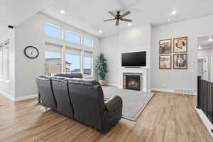 Living area featuring ceiling fan, light wood-style flooring, a stone fireplace, recessed lighting, and a high ceiling