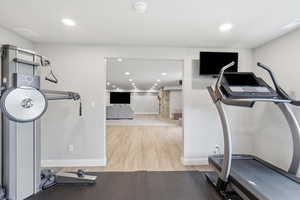 Exercise room with light wood-style floors and recessed lighting