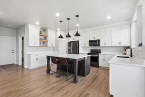 Dual tone kitchen featuring stainless steel appliances, a center island, decorative light fixtures, light wood-style flooring, and a breakfast bar area