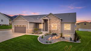 View of front of home featuring board and batten siding, stone siding, a front yard, an attached garage, and driveway