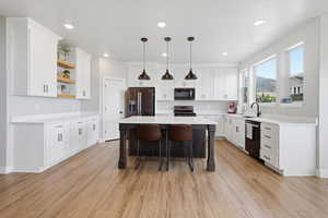 Kitchen featuring a breakfast bar area, a center island, stainless steel refrigerator with ice dispenser, decorative light fixtures, and open shelves
