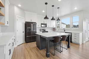 Dual tone kitchen featuring stainless steel appliances, a kitchen island, two tone color scheme, a kitchen bar, and light wood-style flooring