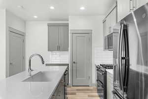 Kitchen with stainless steel fridge with ice dispenser, range with two ovens, recessed lighting, light wood-style flooring, and gray cabinets
