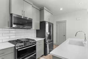 Kitchen featuring stainless steel appliances, gray cabinets, light wood-style floors, decorative backsplash, and modern cabinets