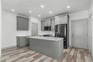 Kitchen with gray cabinets, stainless steel appliances, a center island with sink, decorative backsplash, and recessed lighting