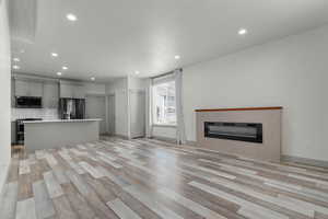Unfurnished living room featuring a glass covered fireplace, light wood-type flooring, and recessed lighting