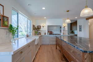 Dual tone kitchen with dark stone countertops, light wood-style floors, pendant lighting, two tone color scheme, and a center island