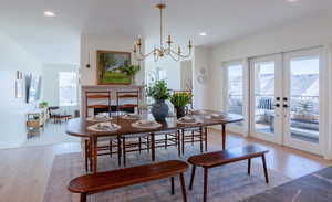 Dining room with light wood-type flooring, french doors, a chandelier, and a fireplace