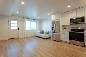 Kitchen with stainless steel appliances, light countertops, white cabinets, recessed lighting, and light wood-style flooring