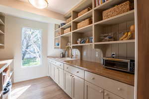 Kitchen with light wood-style floors, butcher block counters, open shelves, and white cabinetry