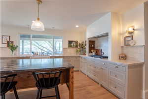 Kitchen with backsplash, light wood-type flooring, dark stone countertops, a kitchen breakfast bar, and decorative light fixtures