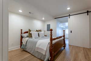 Bedroom featuring a barn door, light wood-style flooring, recessed lighting, and electric panel