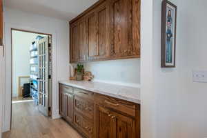 Bar area featuring light wood-style floors, light stone counters, and wood finish cabinets