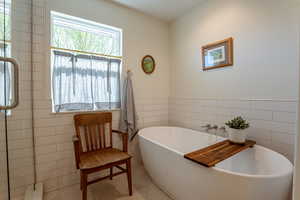 Full bath featuring tile walls, a freestanding tub, a wainscoted wall, and a stall shower