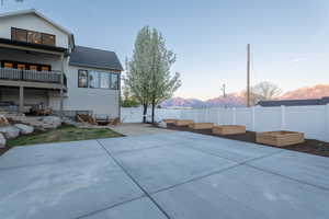 Back of property at dusk featuring a mountain view, a patio, a fenced backyard, a balcony, and a gate