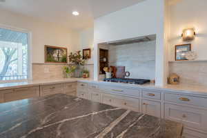 Kitchen with dark stone counters, decorative backsplash, white cabinets, stainless steel gas cooktop, and recessed lighting