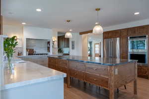 Kitchen with stainless steel appliances, dual tone cabinetry, light wood-style floors, dark stone countertops, and a center island