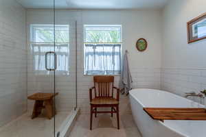Bathroom with tile walls, a stall shower, a freestanding bath, plenty of natural light, and wainscoting