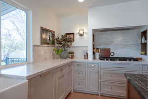 Kitchen with dark stone countertops, gray cabinetry, open shelves, backsplash, and light wood-style floors