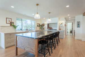 Kitchen with tasteful backsplash, a kitchen bar, dark stone countertops, light wood-style flooring, and pendant lighting