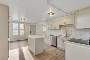 Kitchen featuring a center island, light wood finished floors, backsplash, stainless steel dishwasher, and light stone counters