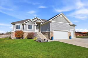 Craftsman-style house with stone siding, board and batten siding, driveway, and roof with shingles