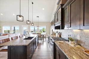 Kitchen with dark wood finish cabinets, a kitchen bar, open floor plan, gas stove, and light stone counters