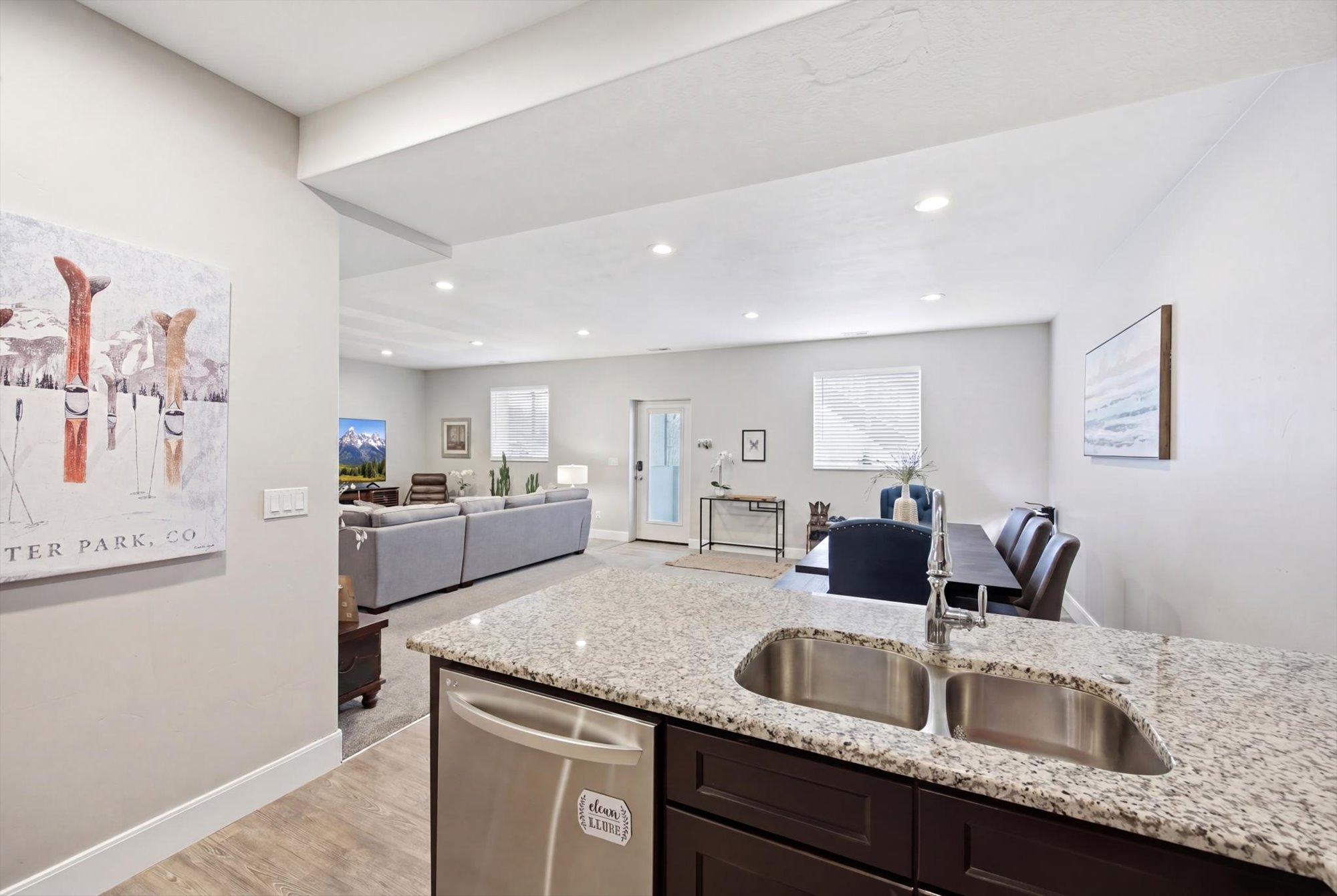 Kitchen featuring open floor plan, stainless steel dishwasher, light stone countertops, light wood-style flooring, and dark wood finish cabinets