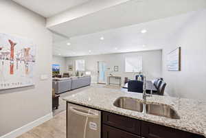 Kitchen featuring open floor plan, stainless steel dishwasher, light stone countertops, light wood-style flooring, and dark wood finish cabinets