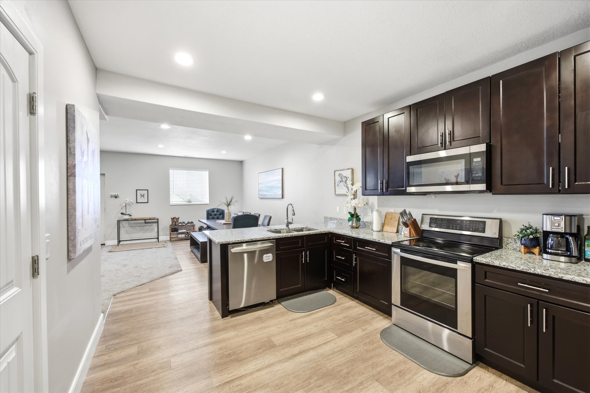 Kitchen featuring stainless steel appliances, a peninsula, open floor plan, light stone countertops, and dark wood finish cabinetry