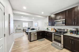 Kitchen featuring stainless steel appliances, a peninsula, open floor plan, light stone countertops, and dark wood finish cabinetry