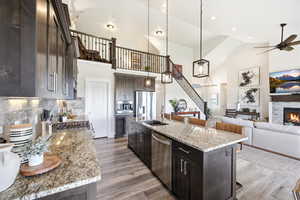 Kitchen with dark wood finish cabinetry, a kitchen breakfast bar, light stone counters, open floor plan, and an island with sink