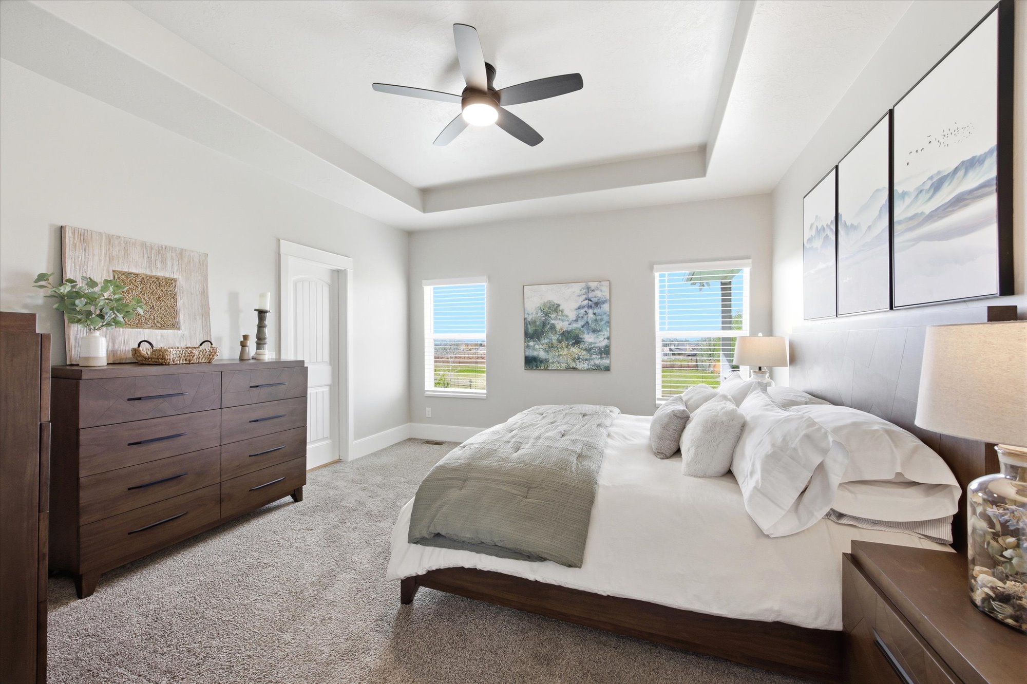 Bedroom with a raised ceiling, light carpet, and a ceiling fan