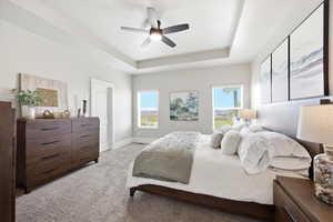 Bedroom with a raised ceiling, light carpet, and a ceiling fan