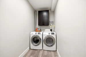 Laundry room with washer and dryer, light wood-style floors, and cabinet space