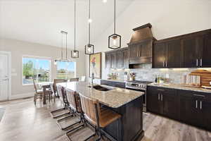 Kitchen featuring vaulted ceiling, light stone countertops, stainless steel gas range, a breakfast bar area, and light wood-style flooring