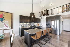Kitchen featuring stainless steel appliances, light stone counters, a kitchen breakfast bar, dark wood finish cabinetry, and an island with sink