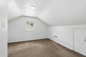Bonus room featuring a textured ceiling and dark colored carpet