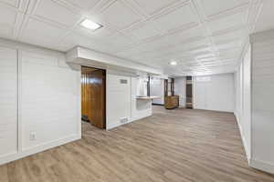 Basement featuring an ornate ceiling, light wood finished floors, and wooden walls