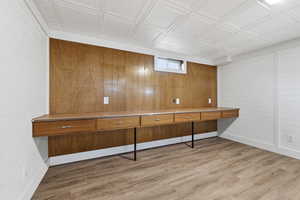 Unfurnished office featuring an ornate ceiling, wood walls, and light wood-style floors