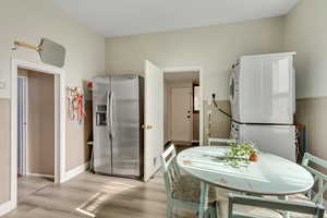Dining room with light wood finished floors, wainscoting, and stacked washer and clothes dryer