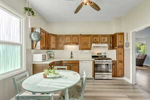 Kitchen with light countertops, white appliances, wood finish cabinetry, light wood-style floors, and ceiling fan