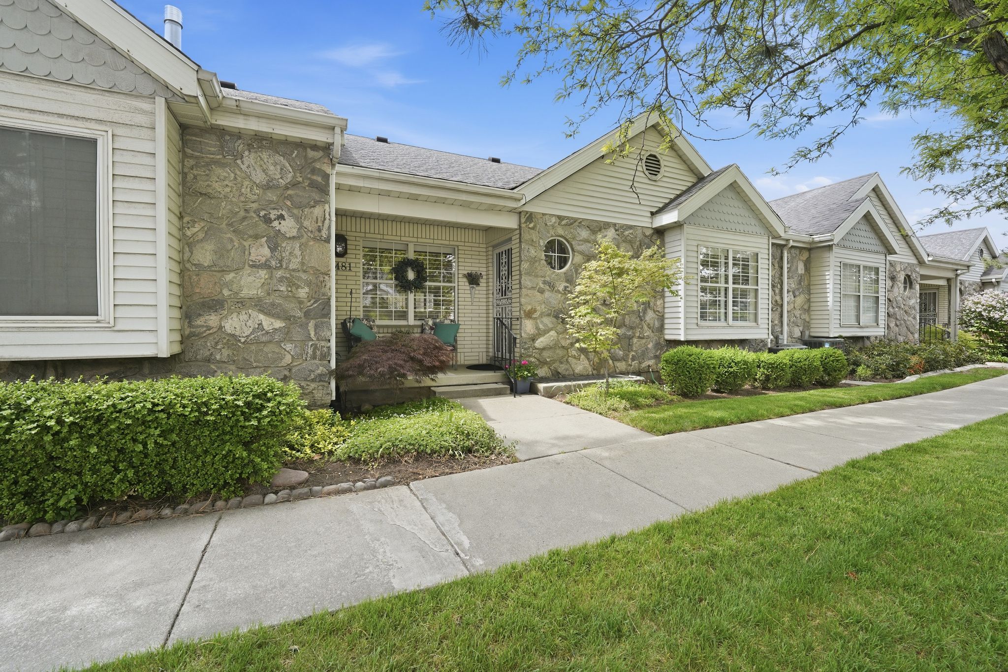 Ranch-style house featuring stone siding, a front yard, a shingled roof, and a porch