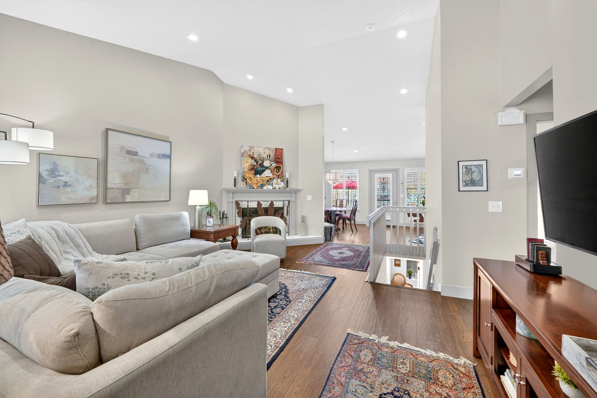 Living room with a fireplace with raised hearth, dark wood-style floors, vaulted ceiling, and recessed lighting