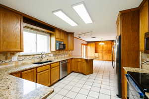 Kitchen featuring decorative backsplash, wood finish cabinetry, light stone counters, a peninsula, and stainless steel appliances