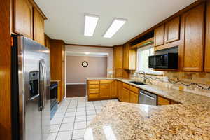 Kitchen featuring black appliances, light stone counters, light tile patterned floors, crown molding, and wood finish cabinetry