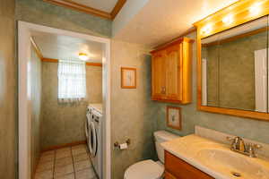Bathroom with vanity, ornamental molding, a textured ceiling, independent washer and dryer, and light tile patterned floors