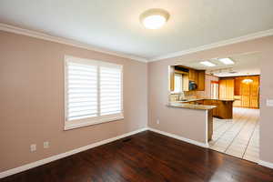 Kitchen with wood finish cabinetry, a peninsula, light wood-type flooring, light stone countertops, and crown molding