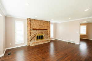 Unfurnished living room featuring healthy amount of natural light, crown molding, dark wood-style floors, a fireplace, and recessed lighting